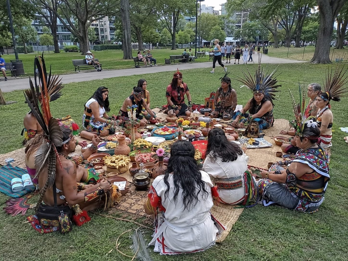 Aztec diners in feathered regalia and woven garments share food from painted pottery on mats in a city park.