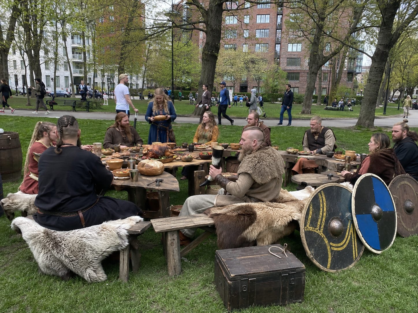 Viking diners in wool, fur, and leather feast at rough wooden tables with shields and drinking horns nearby.
