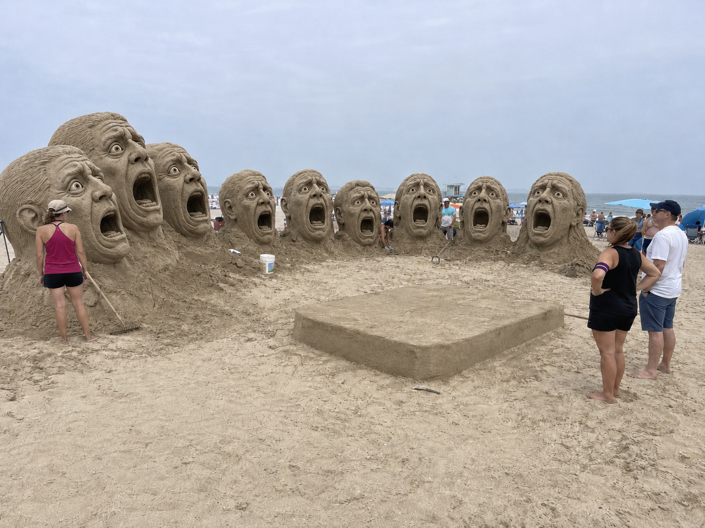 Huge screaming sand heads form a semicircle around an empty conductor platform on the beach.