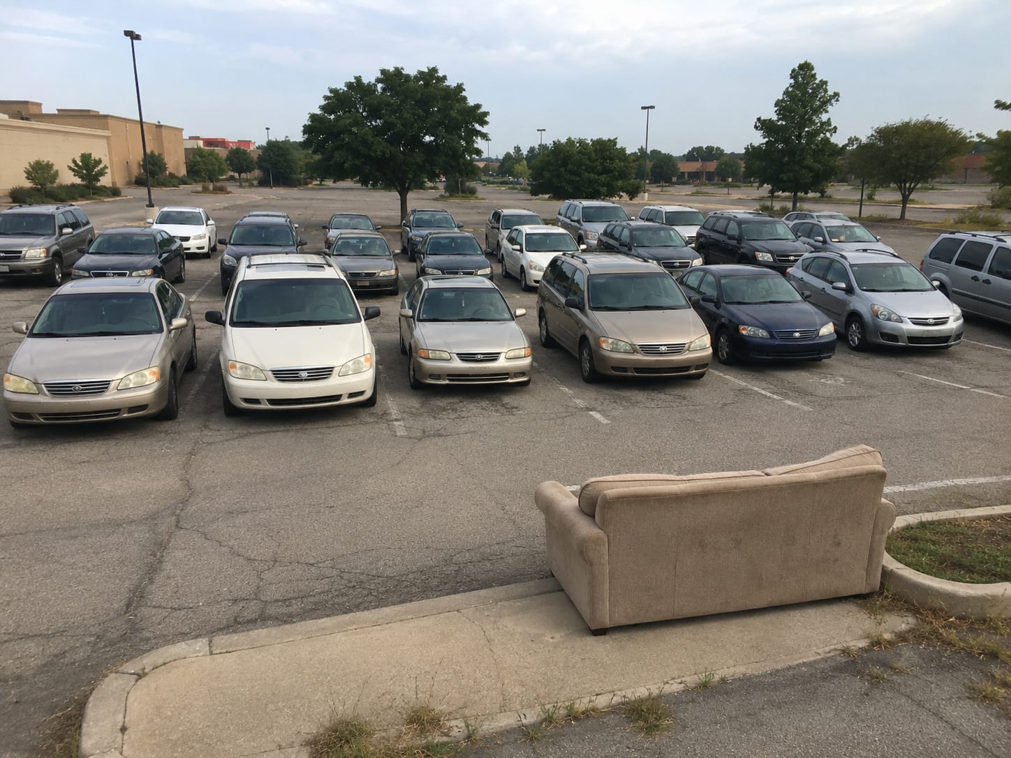 Rows of empty cars face a worn couch in a parking lot, as if waiting for the world’s worst drive-in movie to begin.