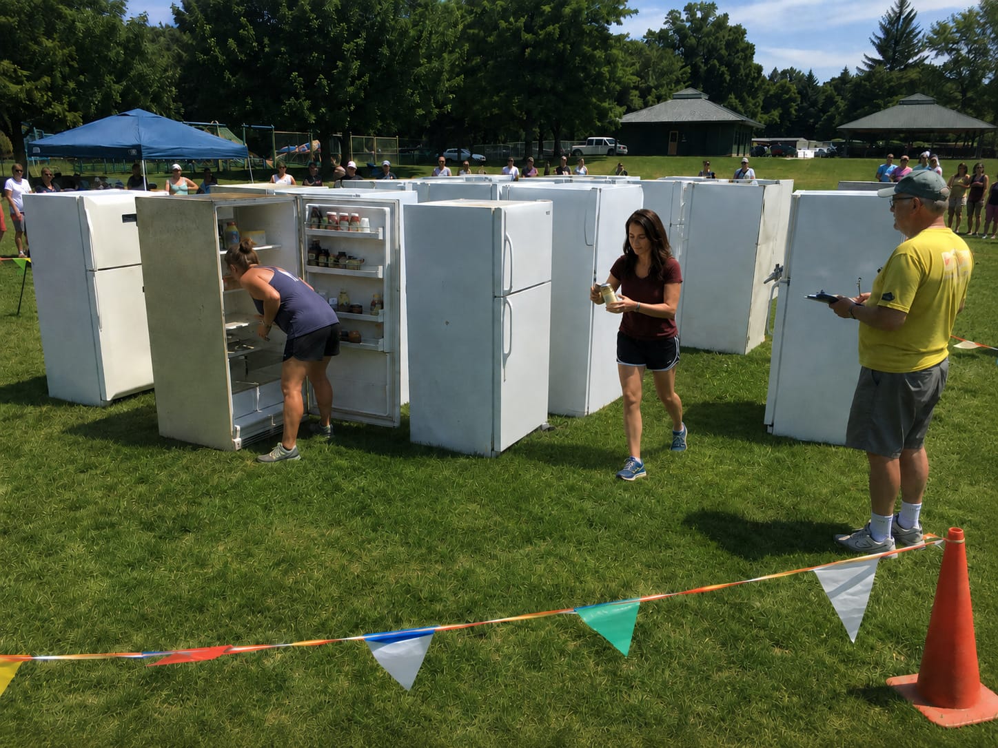 Competitors navigate a maze of open refrigerators on a field, checking contents before moving on.
