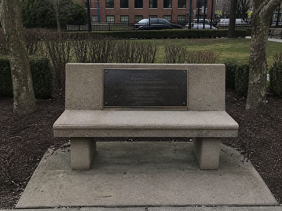 Empty stone memorial bench with a large plaque in a quiet neighborhood park.