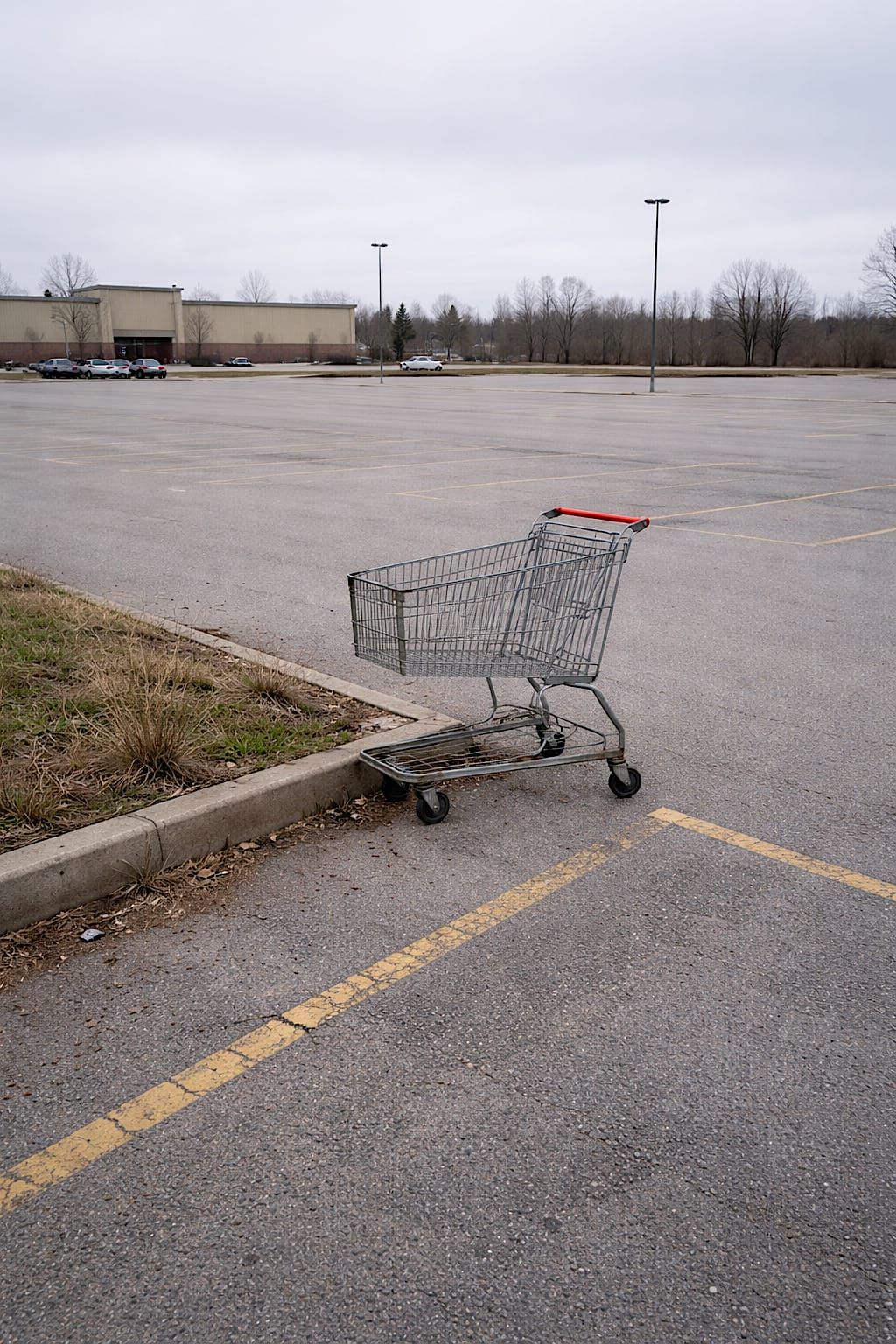 Single metal shopping cart sitting alone at the far edge of an empty parking lot.