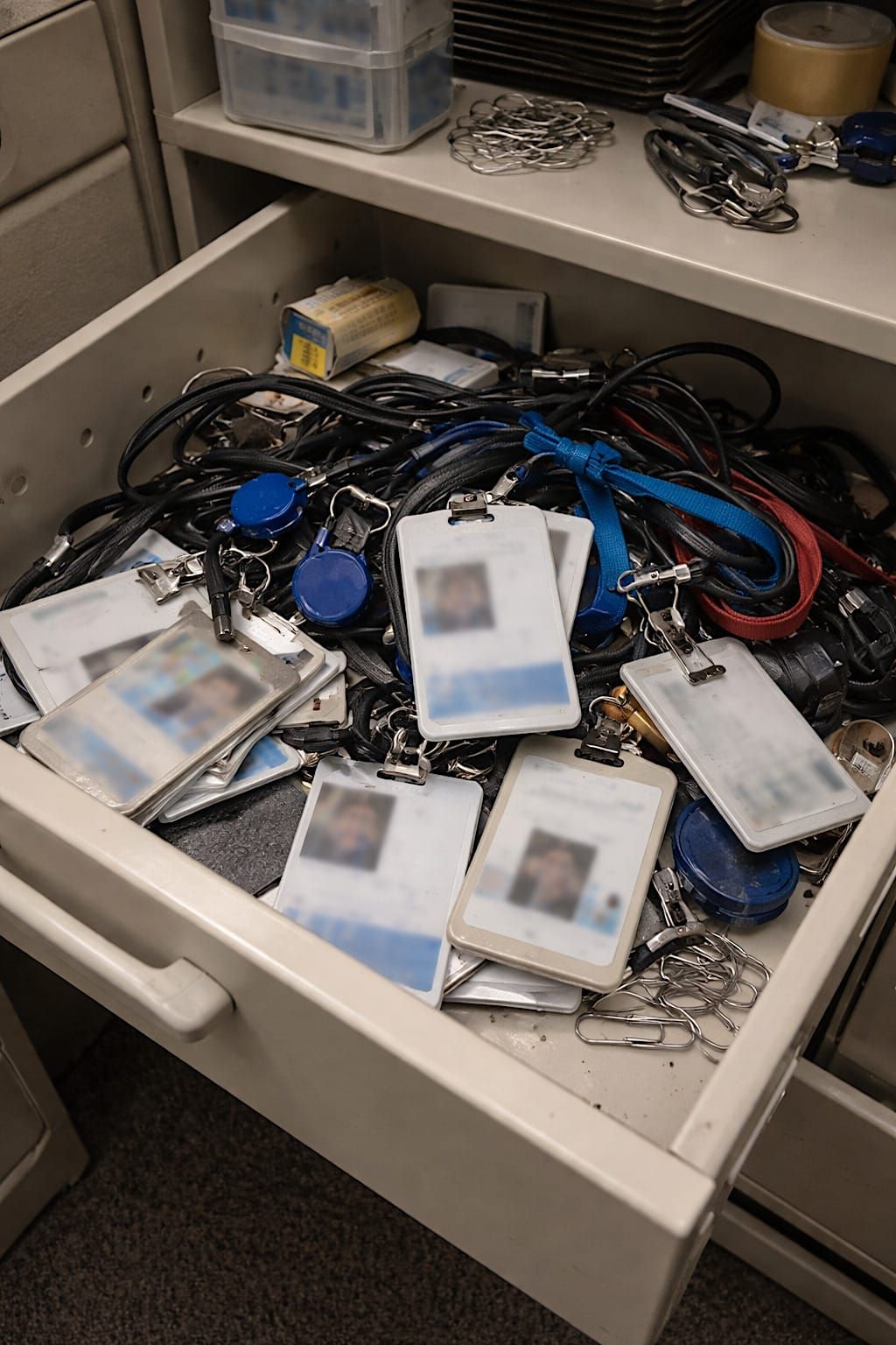 Open office storage drawer filled with old employee badges, lanyards, access cards, and badge reels.