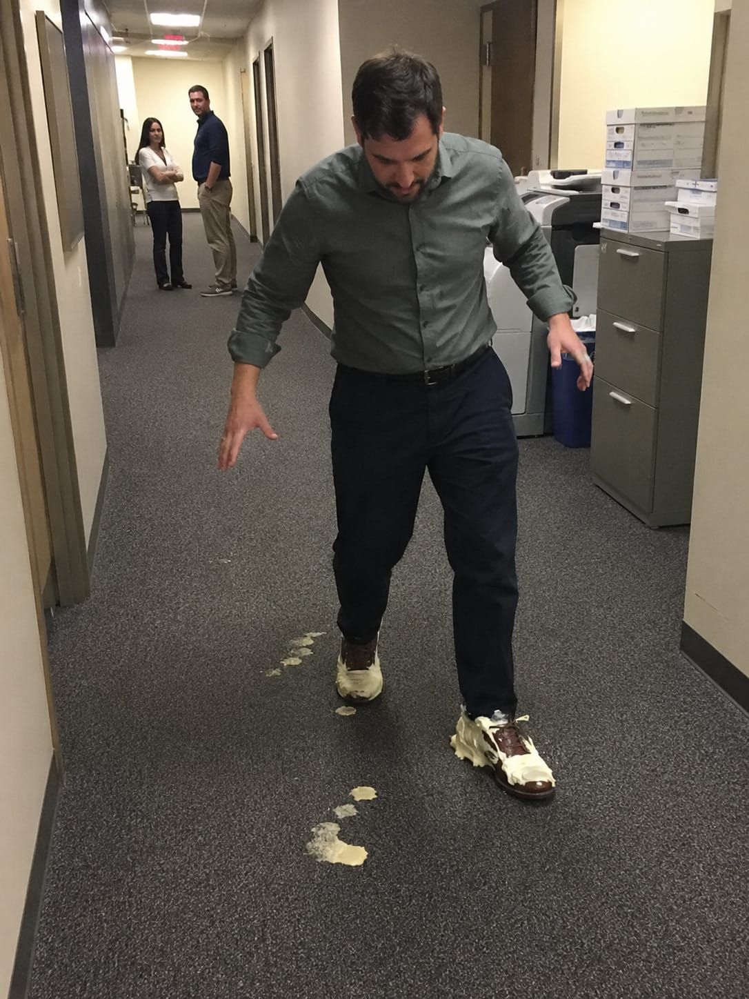 Office worker walks carefully down a hallway in dress shoes filled with vanilla pudding while coworkers avoid eye contact.