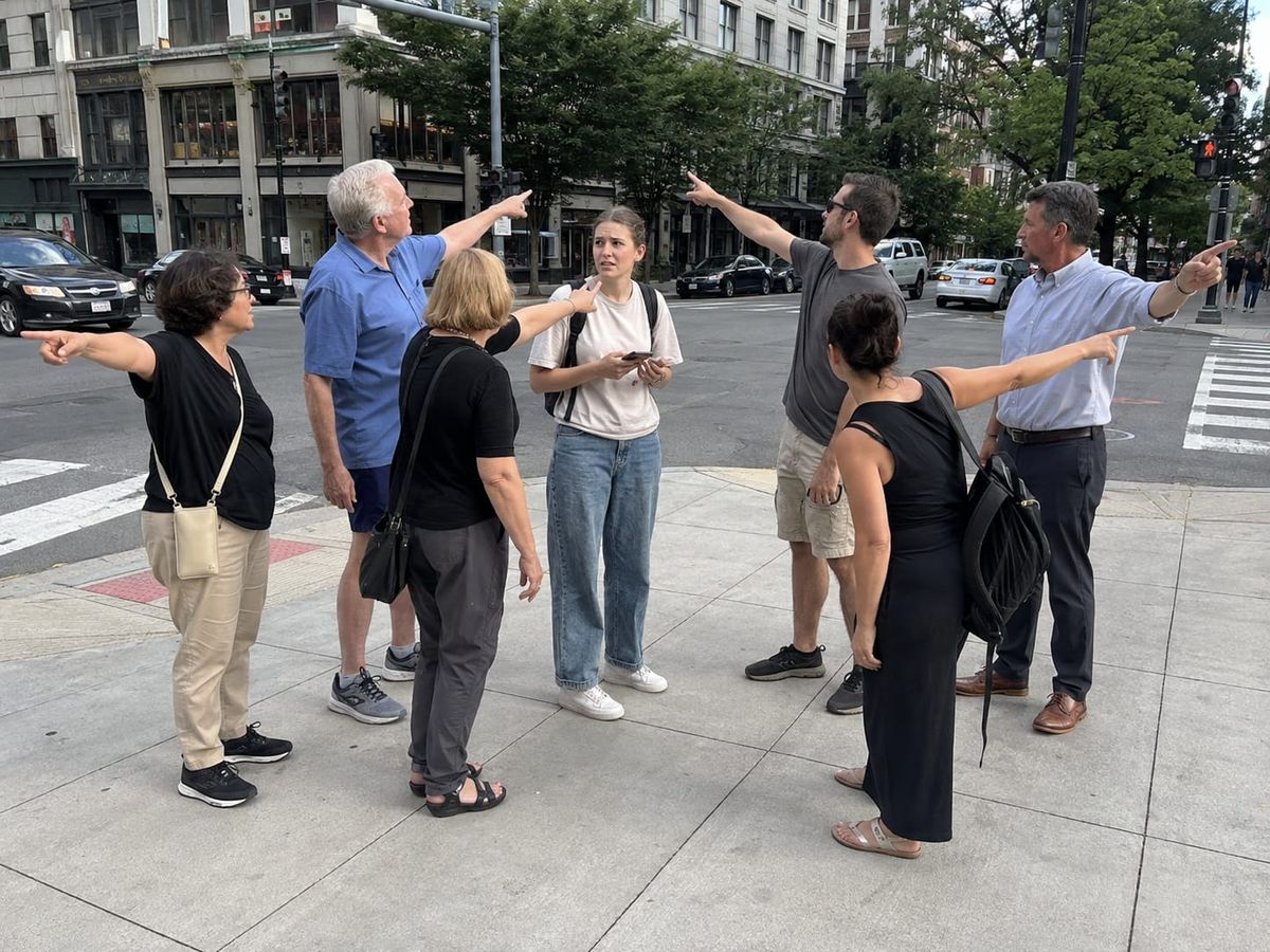 Confused tourist at a city intersection surrounded by six people simultaneously pointing in different directions.