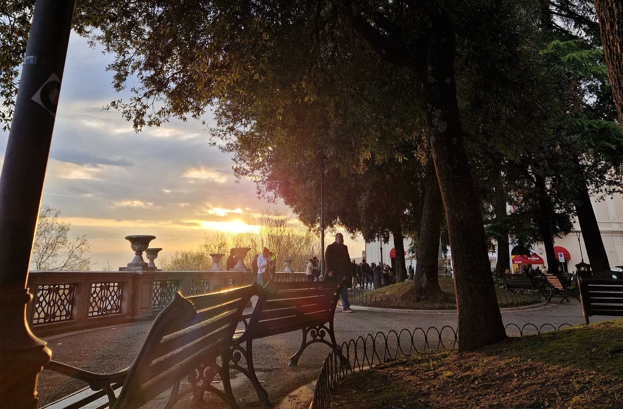 The sun setting over a park. In the distance journalists can be seen talking.