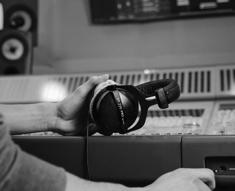 a black and white photo of the DT 770 headphones taken in a recording studio with an out of focus mixing board in the background