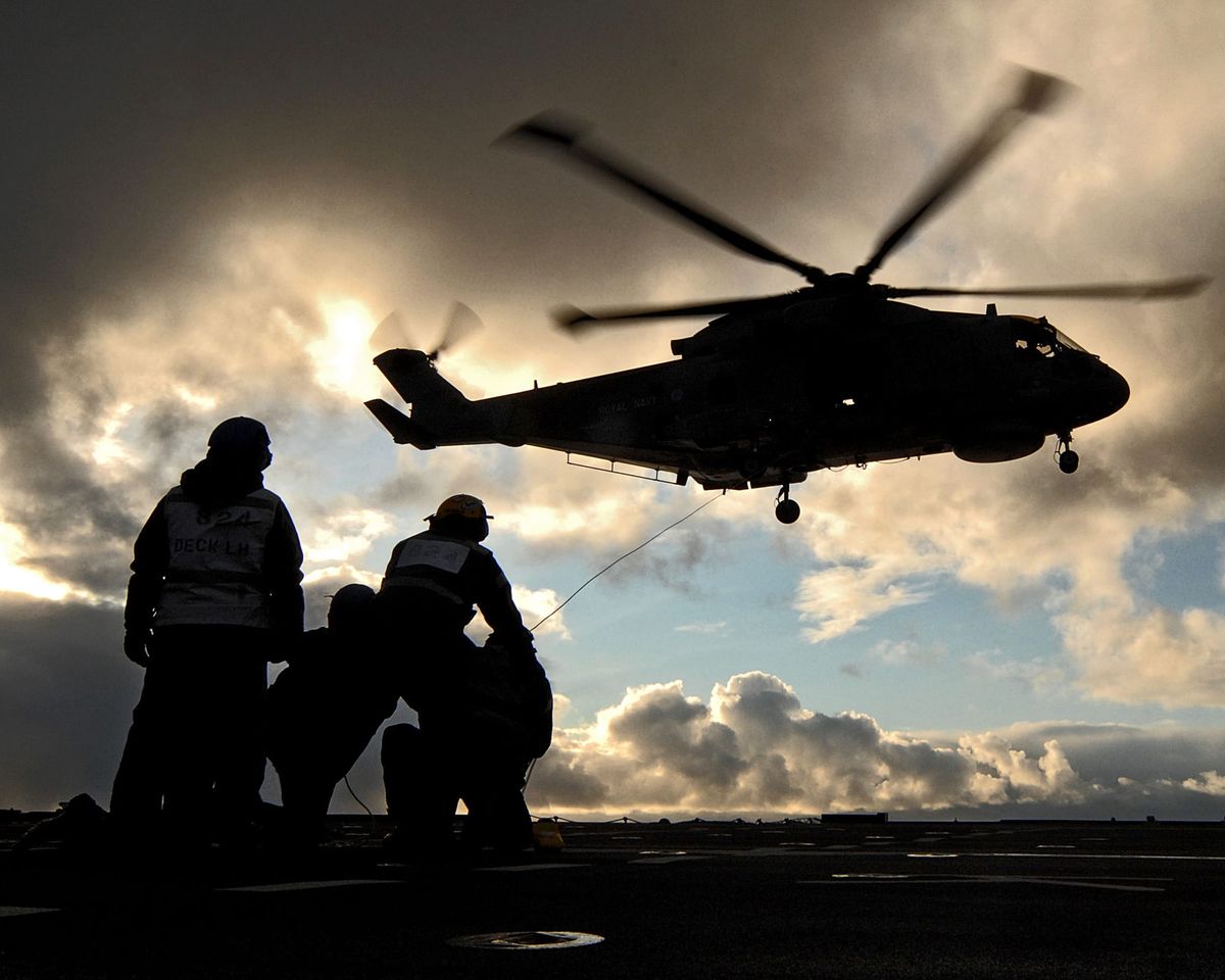 Helicóptero Merlin de la Royal Navy a contraluz sobre la cubierta de un buque
