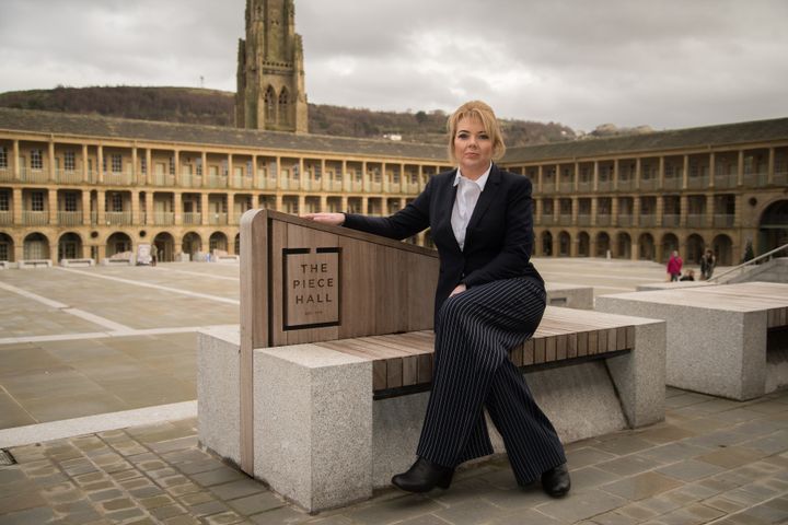 A woman in a dark suit sitting in the courtyard of The Piece Hall in Halifax.