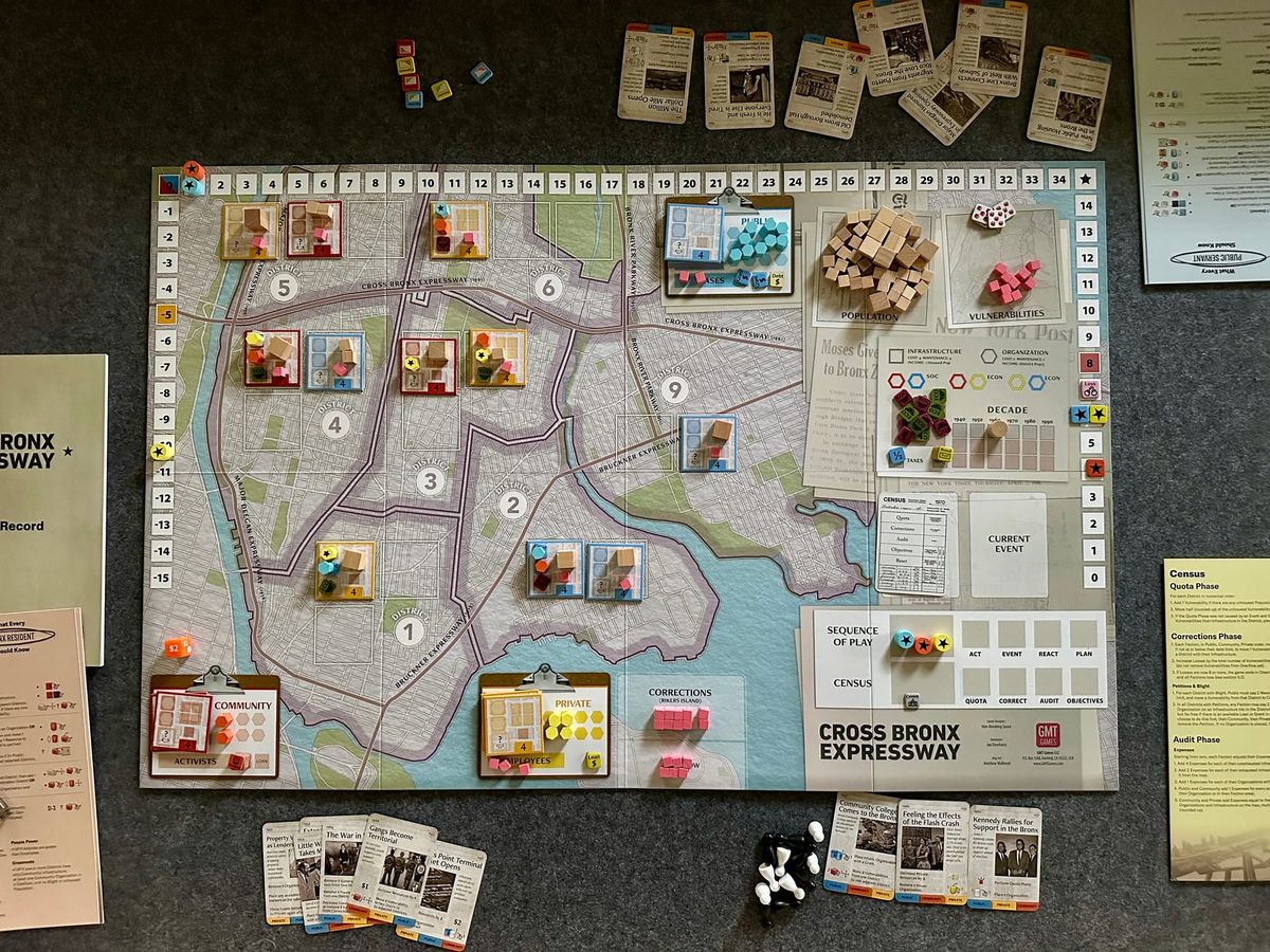 View from above at the board game Cross Bronx Expressway. Wooden pieces in multiple colors, cards detailing historical events, and tokens to track board state. 