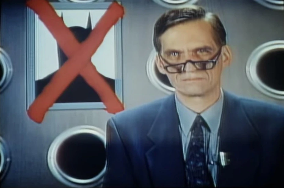 Merle Kessler playing news anchor Kenneth Frequency in "Batman Forever." He is peering over his glasses, with an image over his shoulder of a Batman silhouette covered by a red X. That movie sure did suck.
