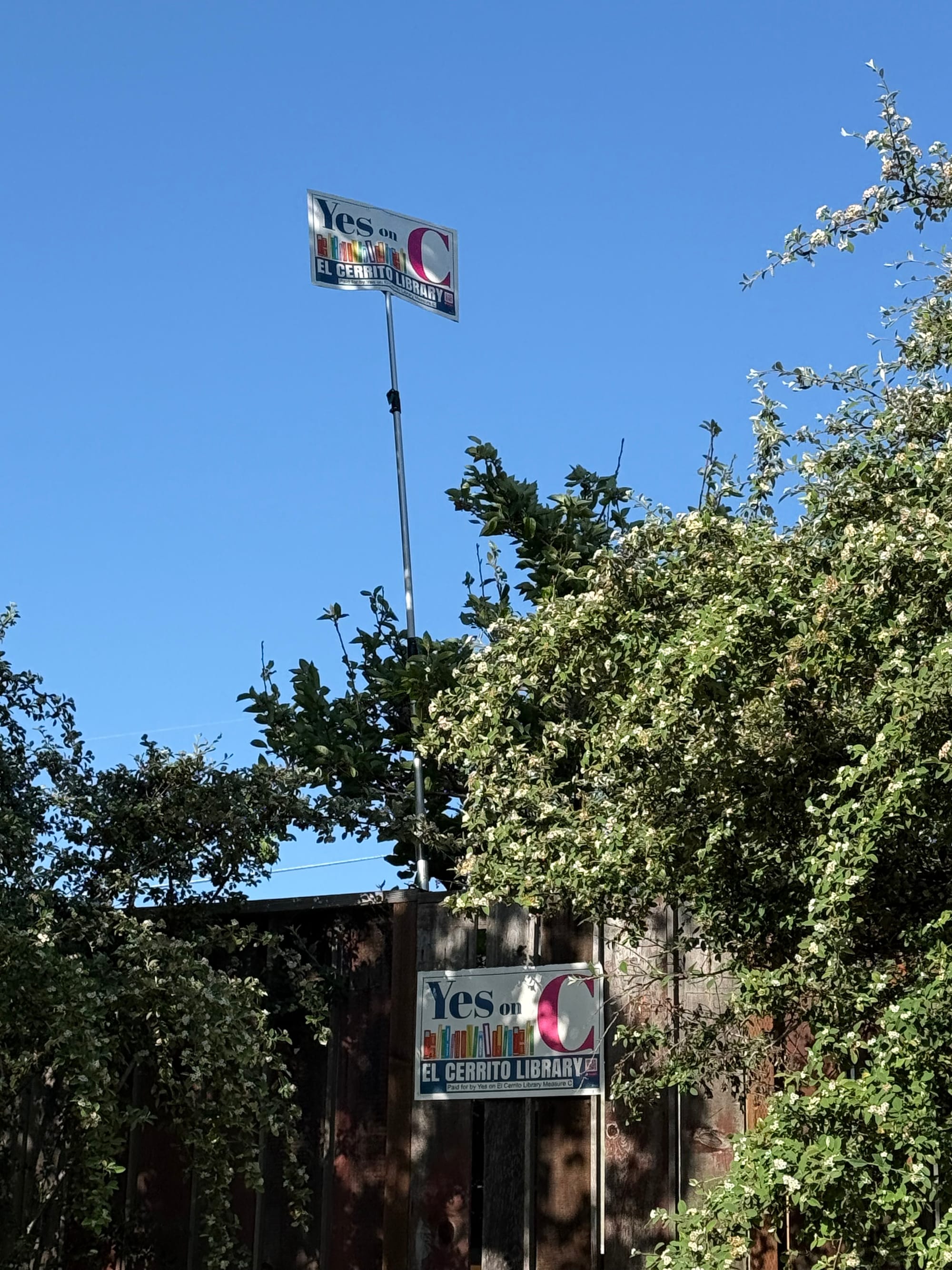 "Yes on C" signs, one attached to some brown fencing, the other on a pole flying above the fence.