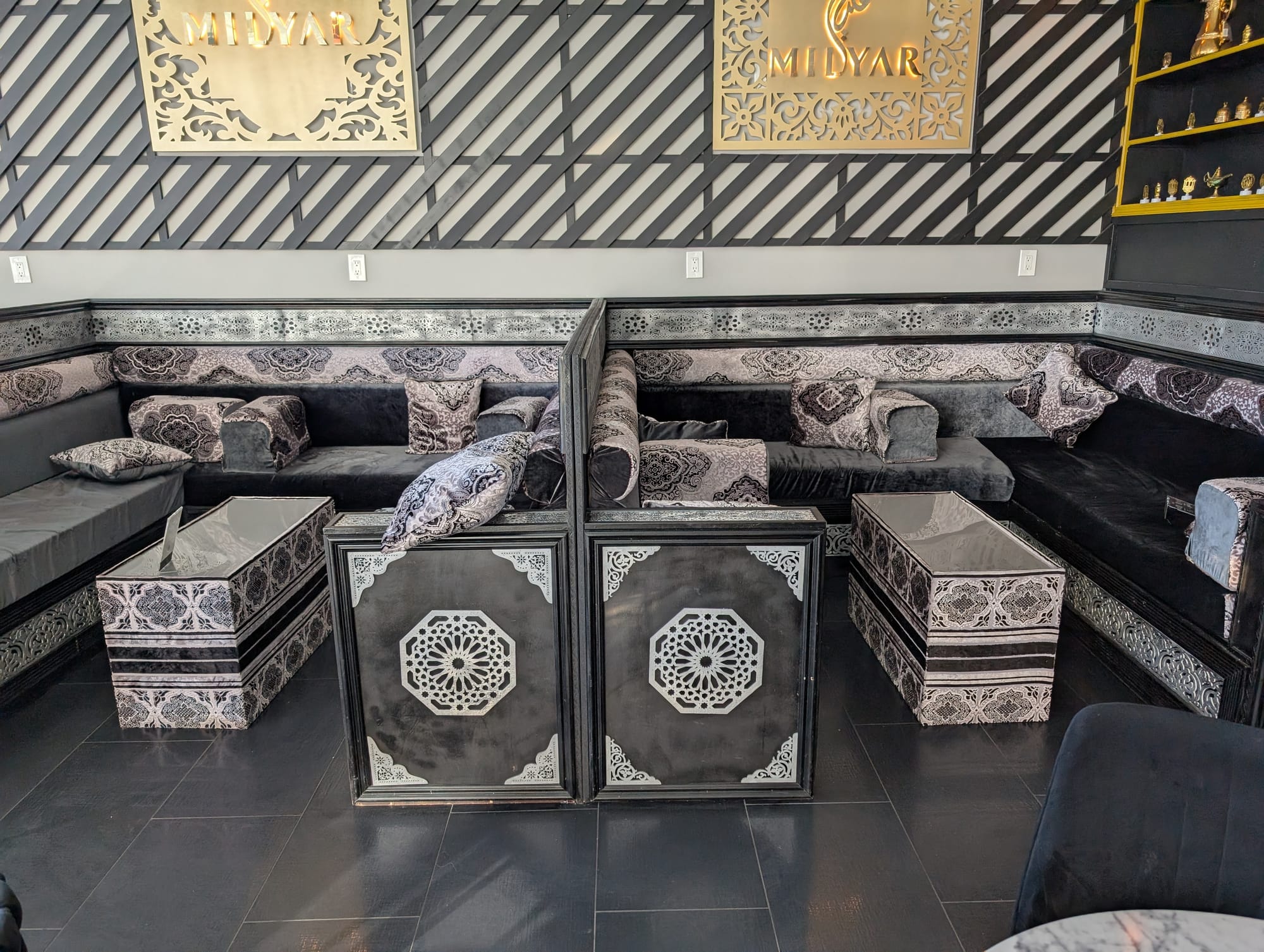 Booth-style seating with detailed paneling and patterned fabric covering plush cushions and pillows. The design is intricate but strictly black and white, with some golden finishes on the wall.