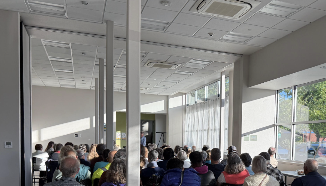 A photo of the meeting, with afternoon light slanting in through the windows just above the heads of the people in attendance.