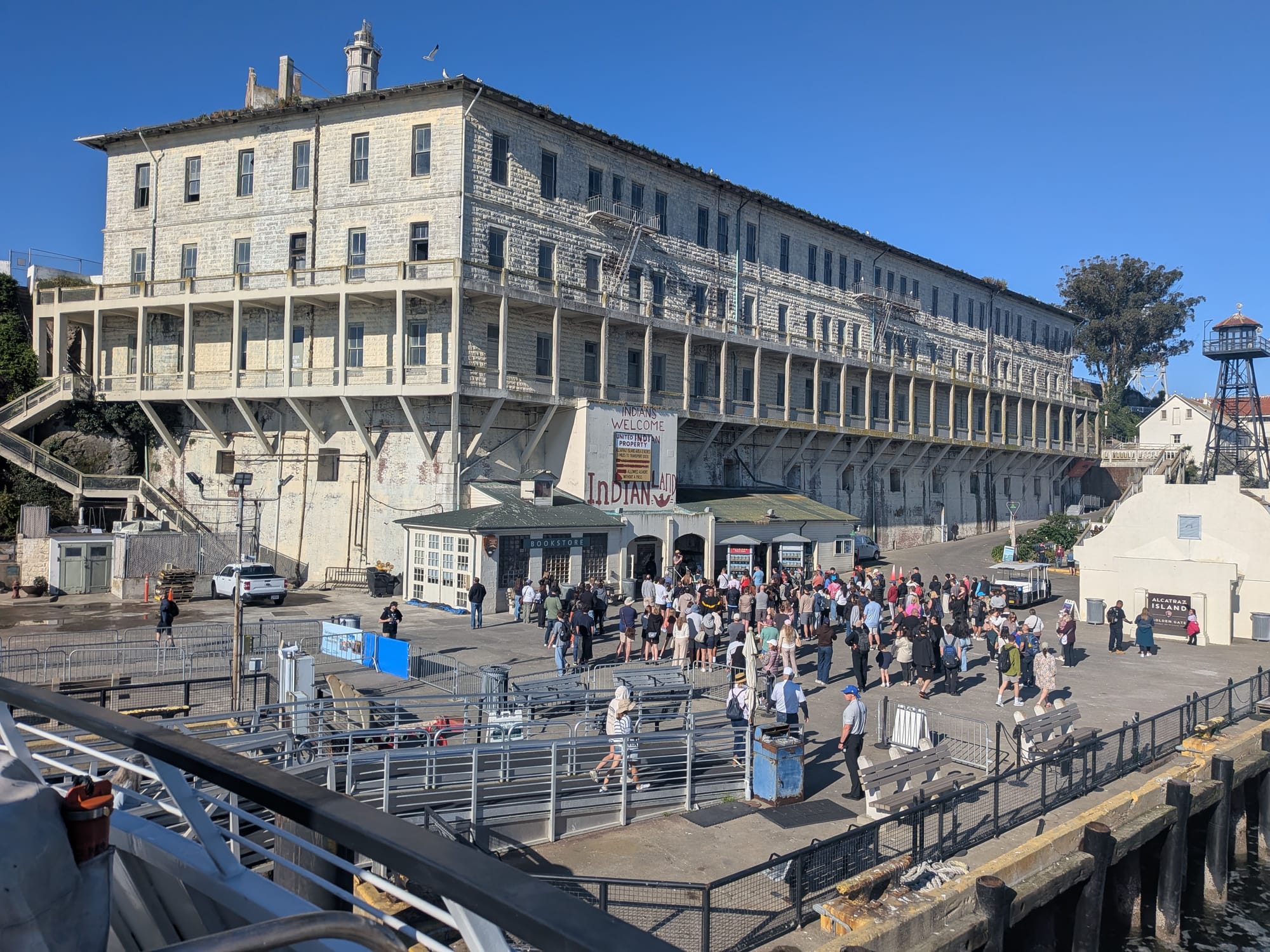 Tourists milling around the entrance to Alcatraz, with a sign above reading "INDIANS WELCOME" and "INDIAN LAND."