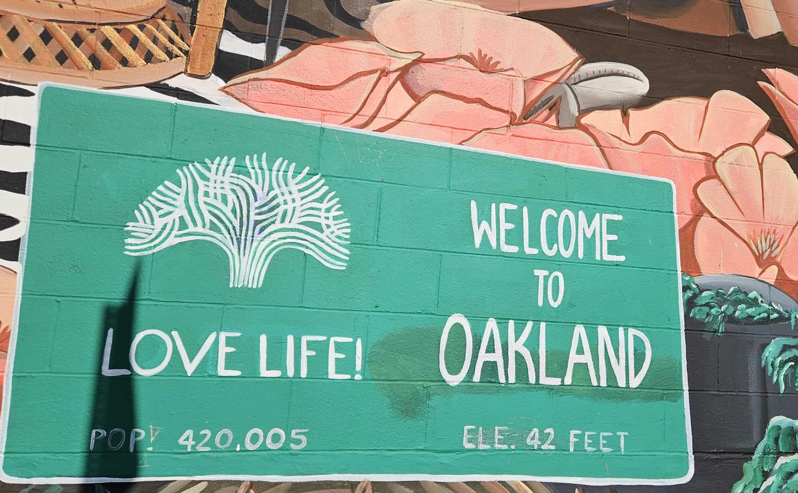 A "Love Life! Welcome to Oakland" sign, painted on a wall in the style of a street sign