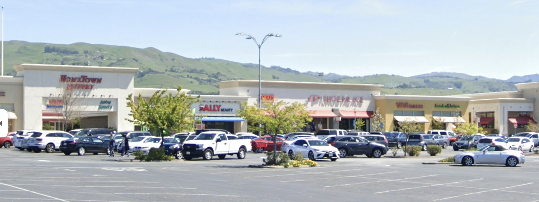 an exceedingly normal strip mall, parking lot, hills in the background