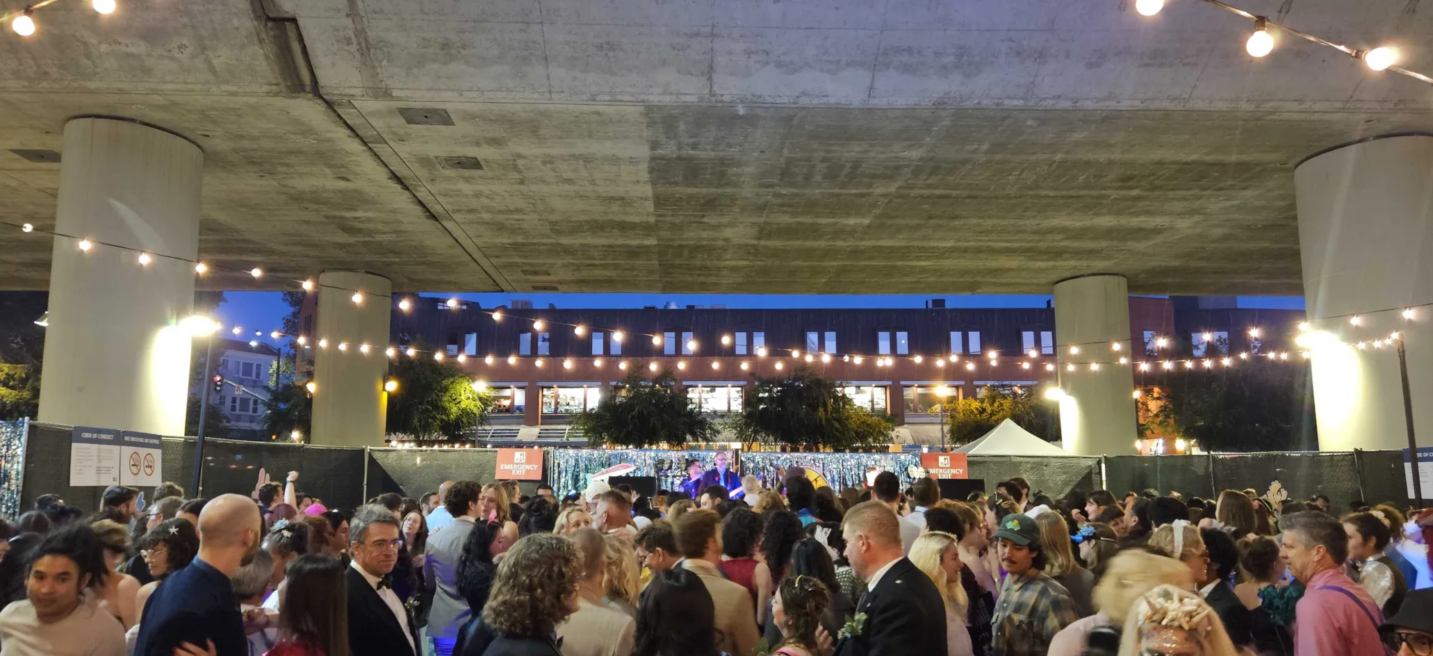 Dancers under the BART tracks, lights and costumes, sunset