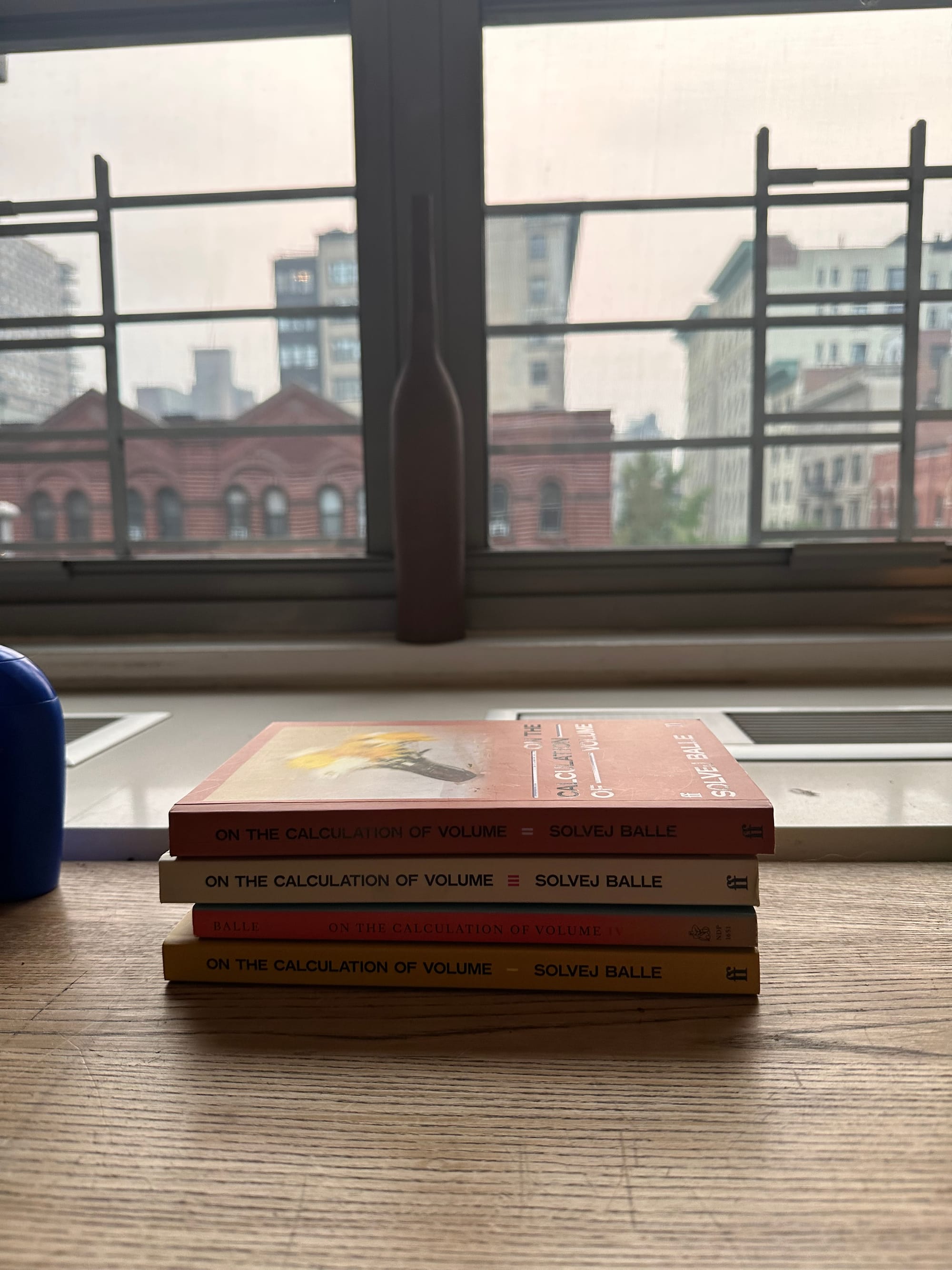 four books on a wooden desk, with a view of the city, from a slightly different angle, all stacked neatly now.