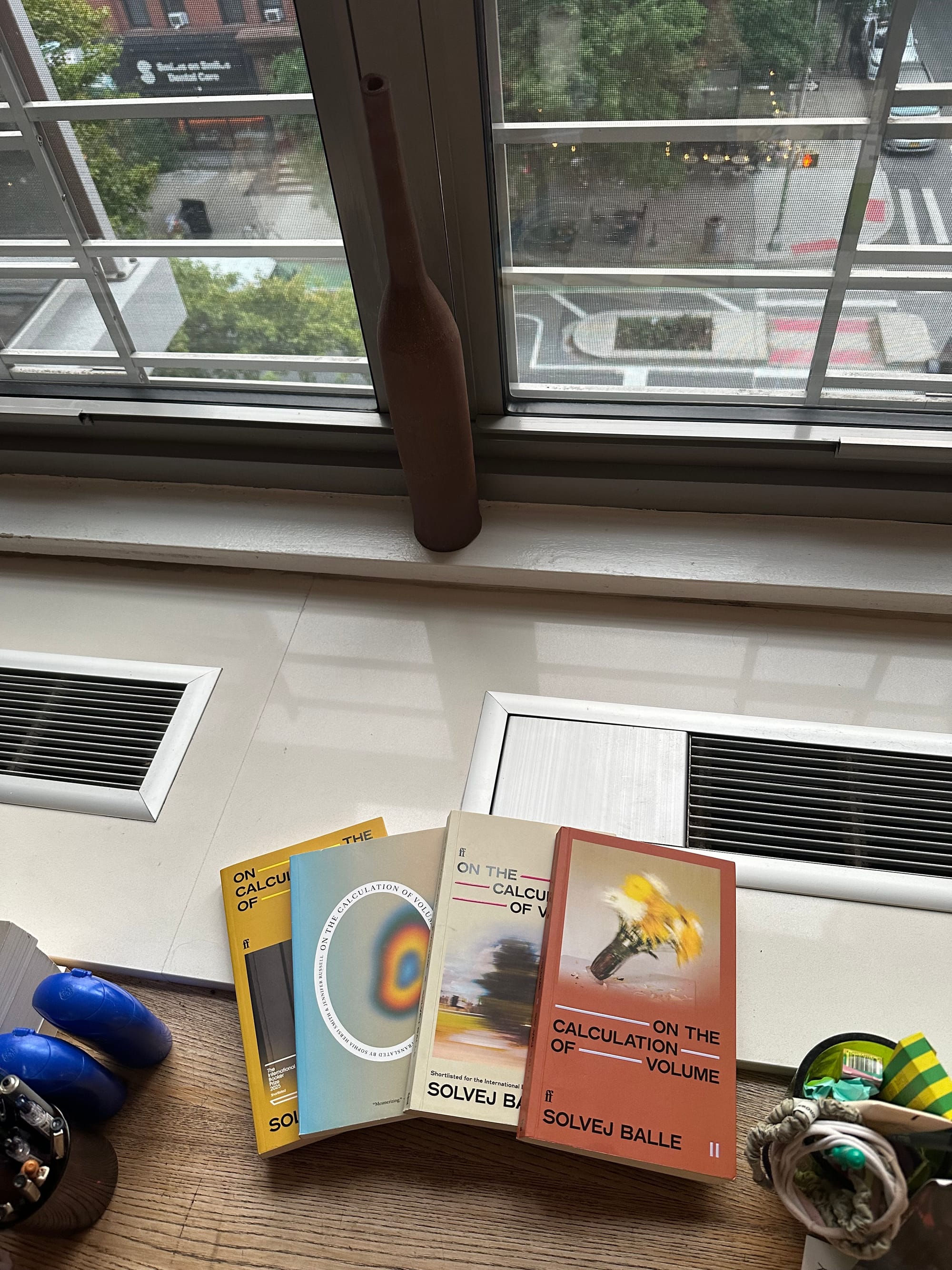 four books on a wooden desk, with a view of the city, from a slightly different angle, and brighter now.