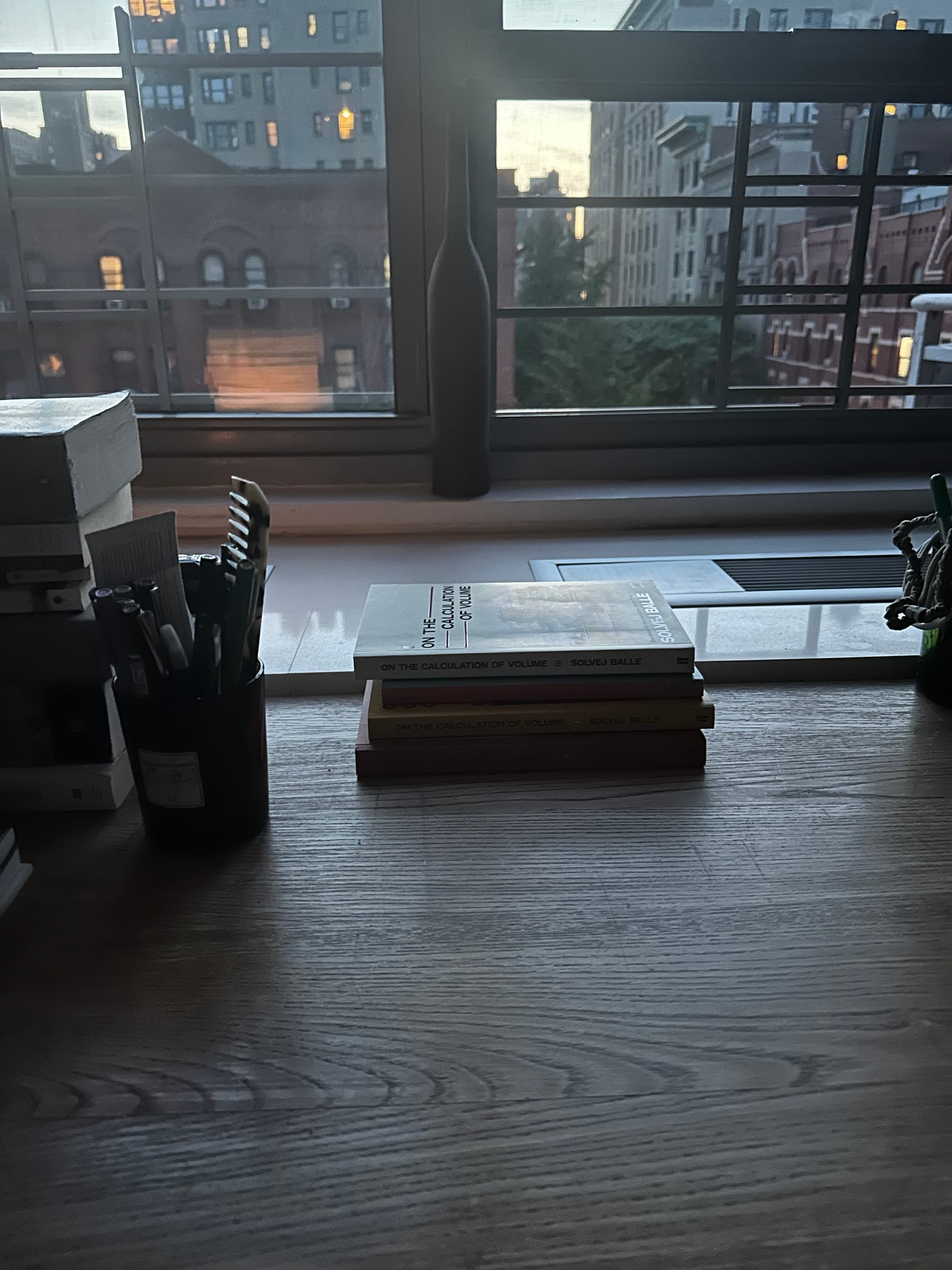 four books on a wooden desk, with a view of the city, silvery light.
