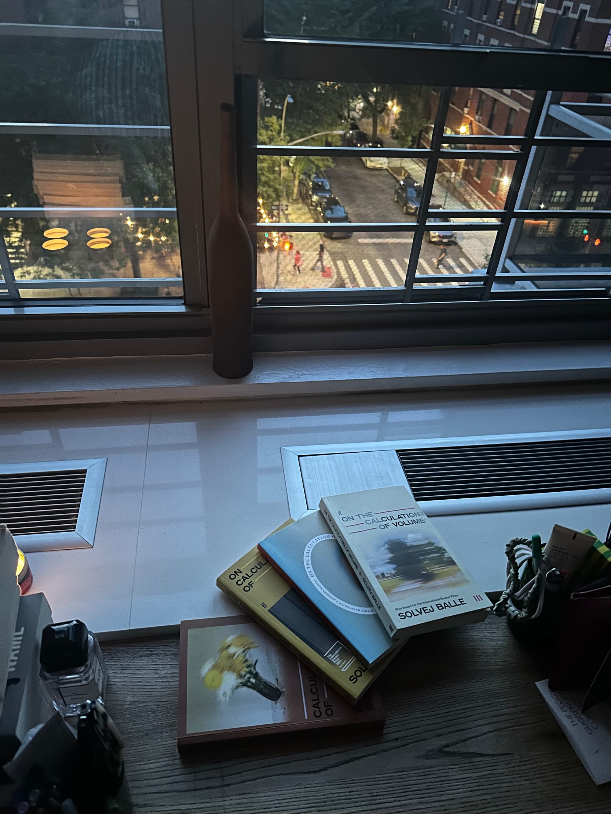 four books on a wooden desk, with a view of the city, from a slightly different angle, and darker now.