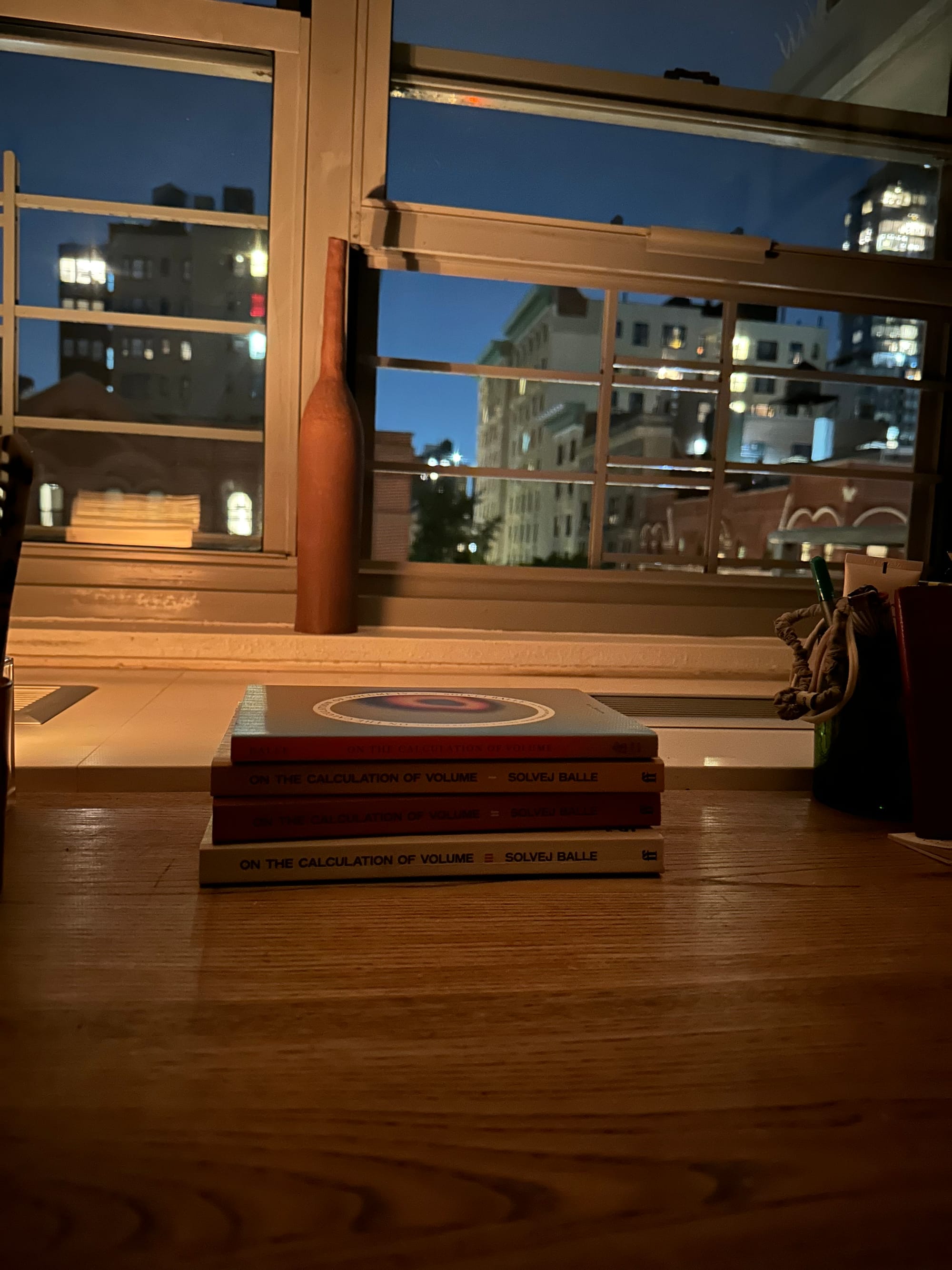 four books on a wooden desk, with a view of the city, from a slightly different angle, and darker now.