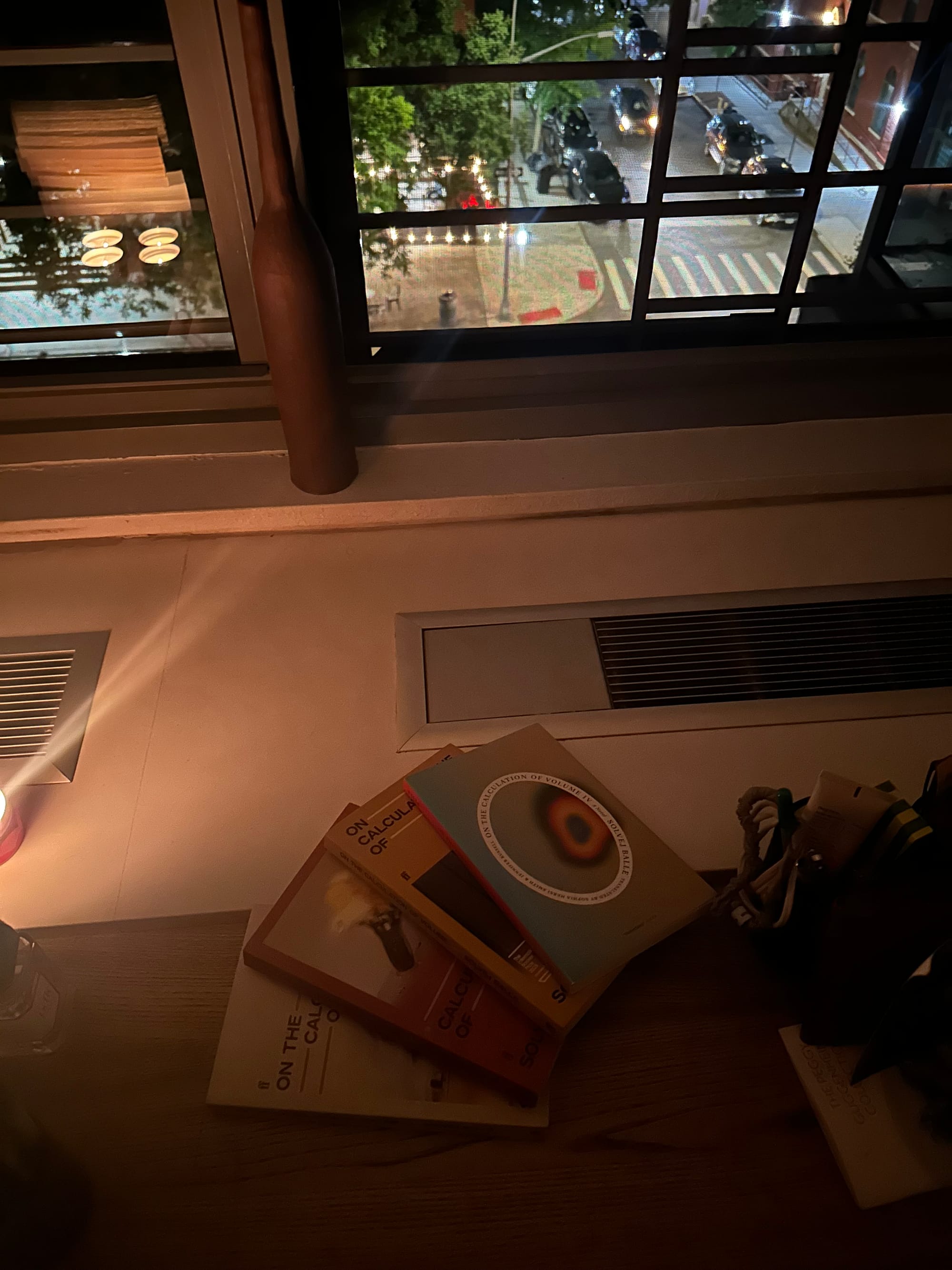 four books spread on a wooden desk, with a view of the city, from a slightly different angle, and darker now.