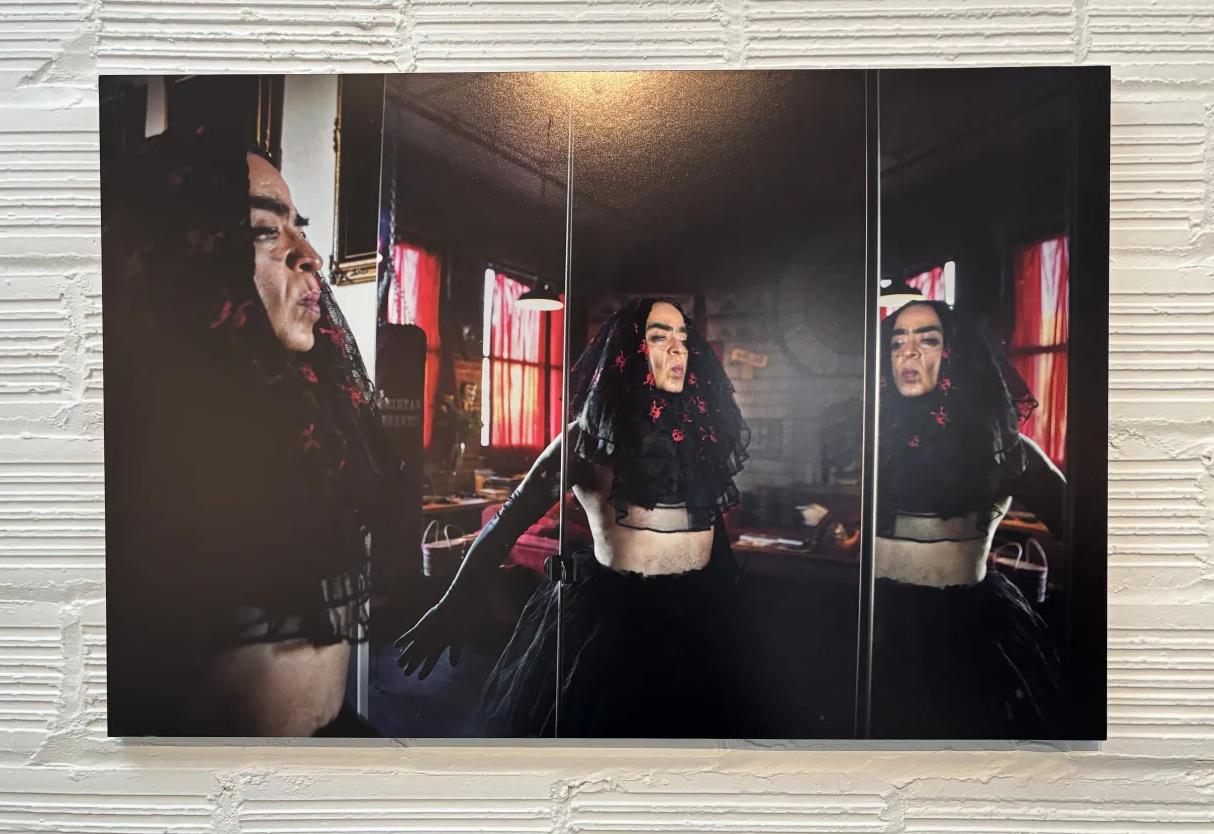 image of GP standing serene in an elaborately-embroidered dark veil in front of a mirror so that we see an image of GP in triplicate.