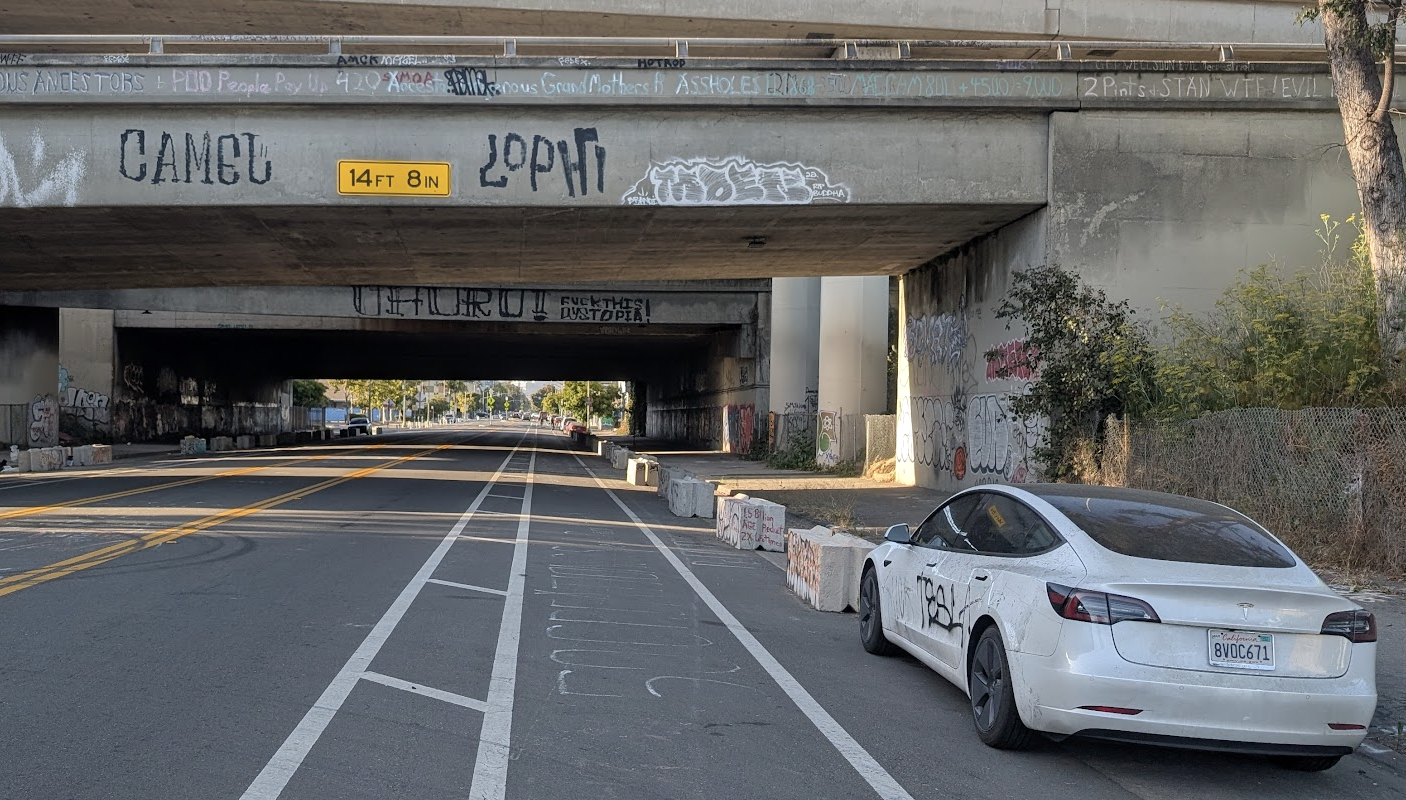 an overpass, heavily tagged, with caravan gravestones and an abandoned and tagged Tesla.