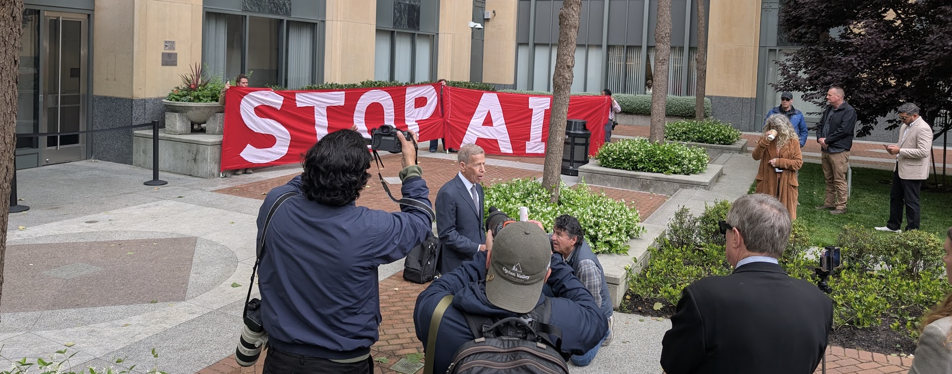 A large STOP AI banner behind the lawyer speaking to microphones and cameras.