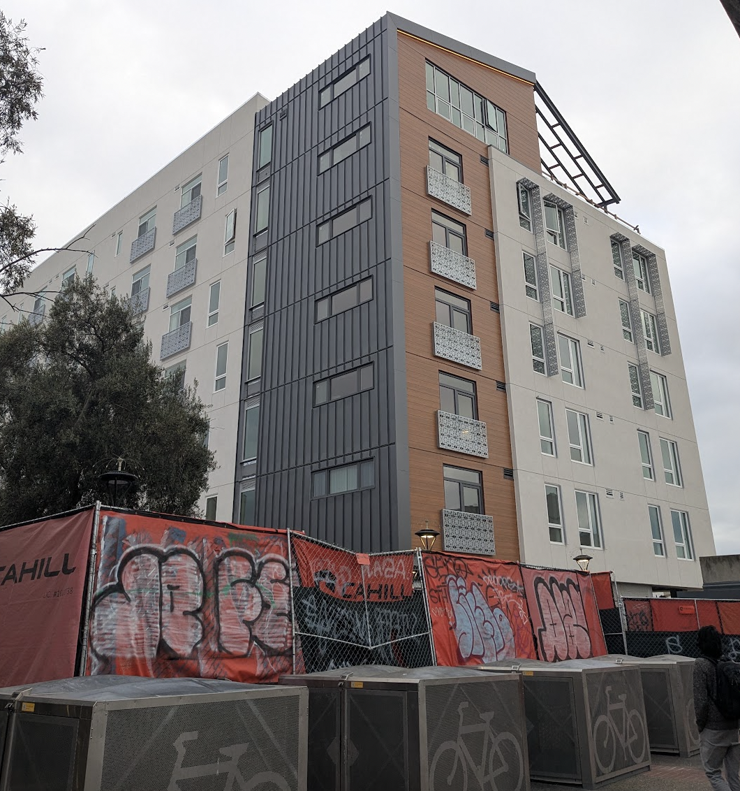 A new building rising up out of layers of fencing and biicycle parking. (MS)