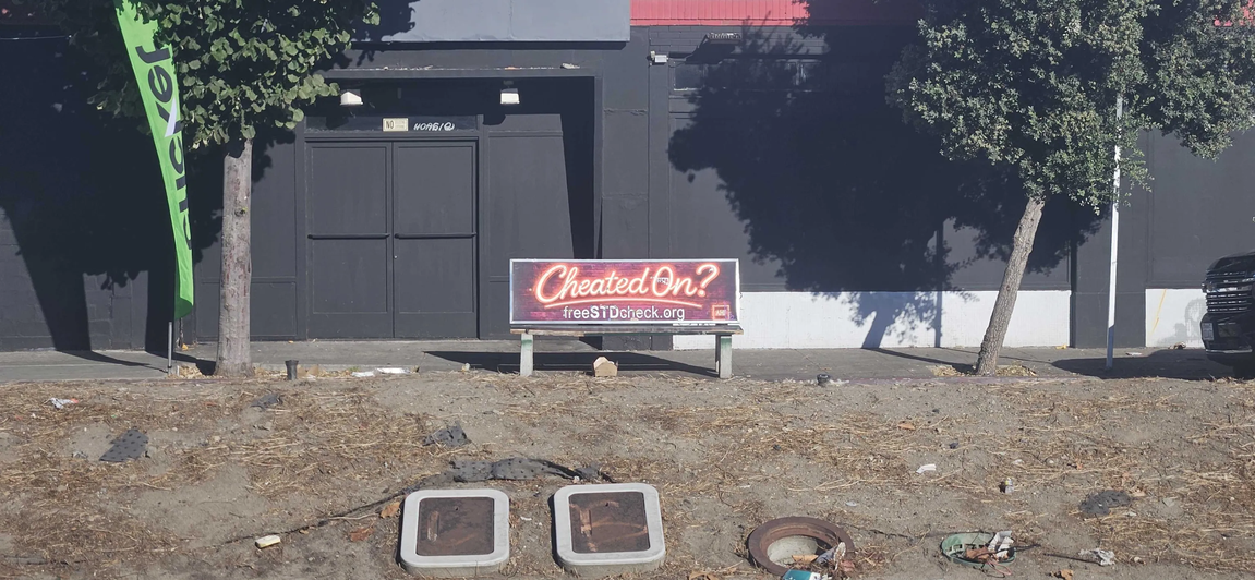 A bench, with an ad on it for free STD testing, the text reading "Cheated On?"