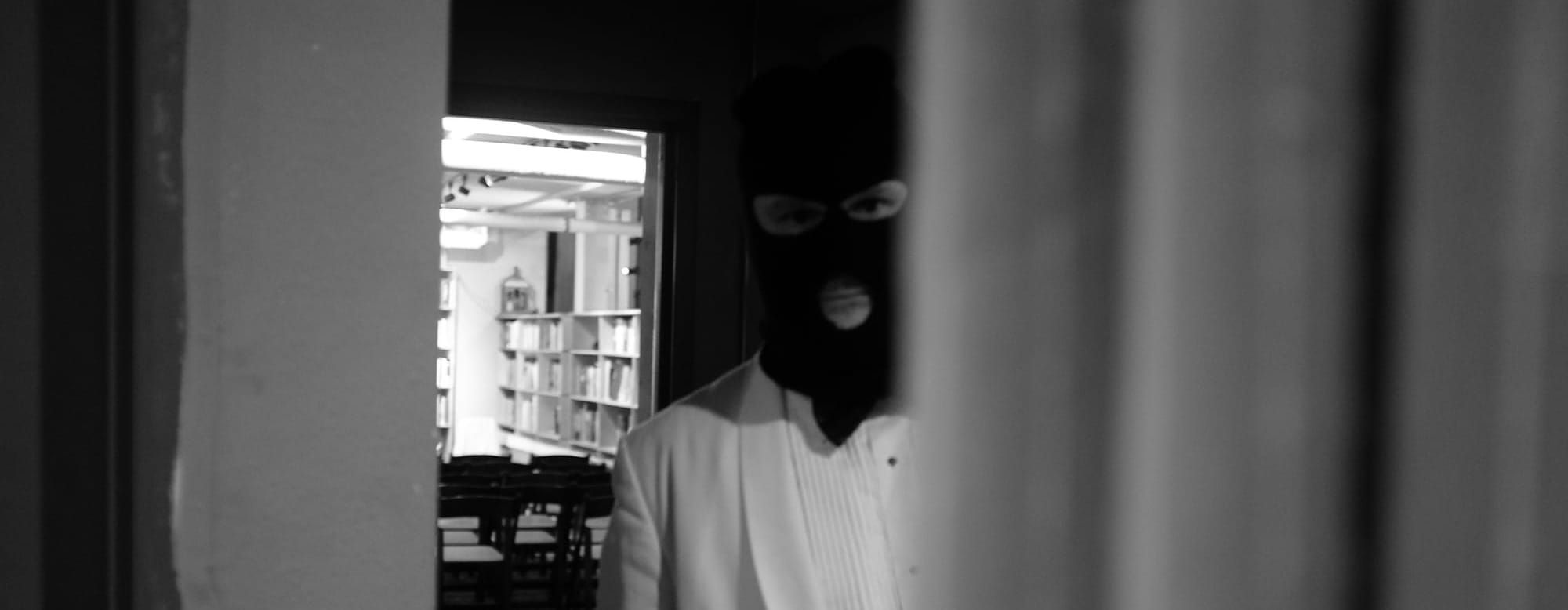 An actor in a tux and a ski mask, looking ominously at the viewer.