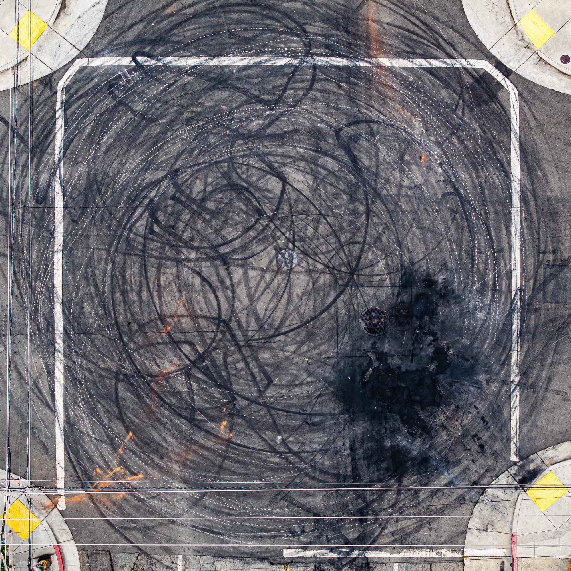 An aerial view of an Oakland intersection in the aftermath of a sideshow, with rings of black skidmarks. 