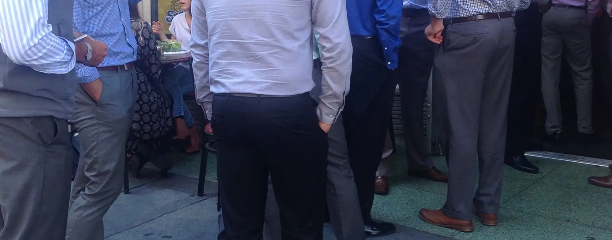 A photo of men in very 2015ish downtown SF business dress—gray pants, check shirts, vests. They're waiting in line outside a restaurant.