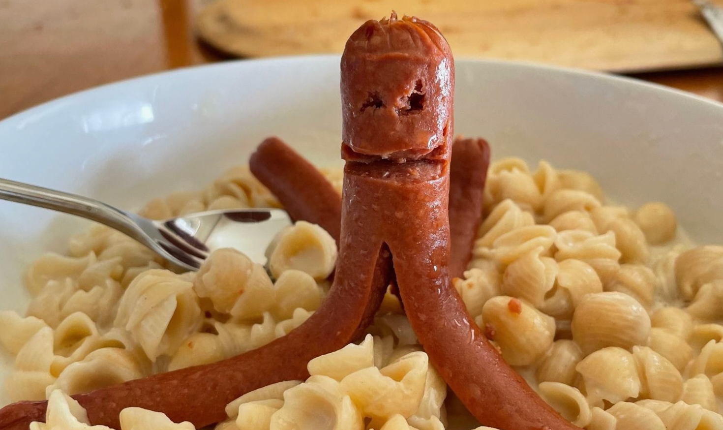 a hot dog cut into a creature, perched atop a plate of mac-n-cheese