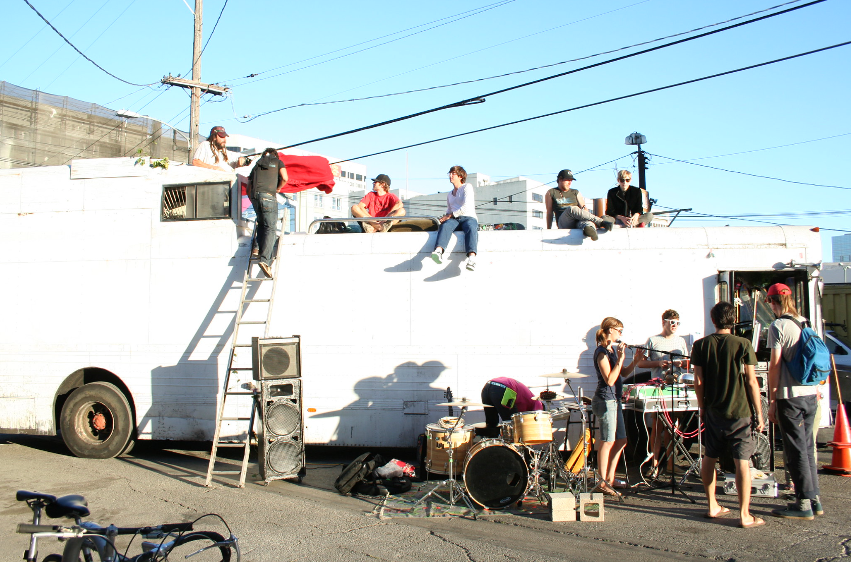 People sitting on a repainted white bus, musical instruments and equipment in the foreground