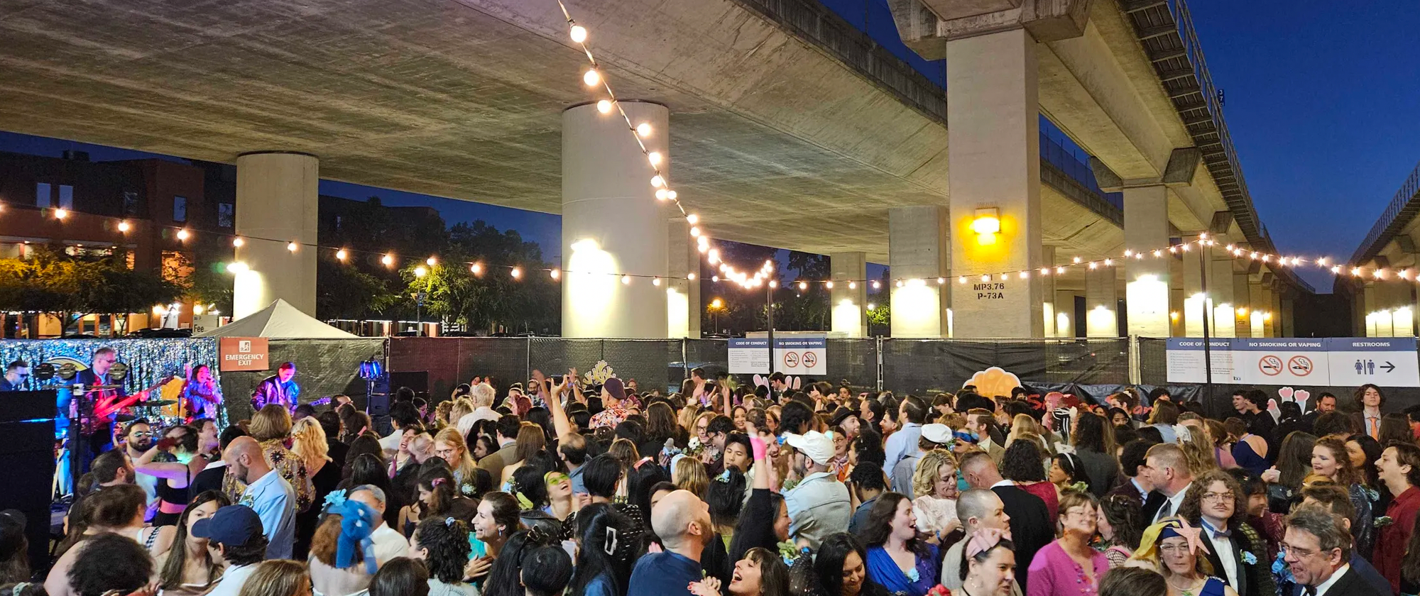 Dancers under the BART tracks, lights and costumes, sunset