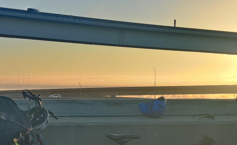 a blue helmet on the side of a bridge overlooking the ocean and yellow sky at sunset