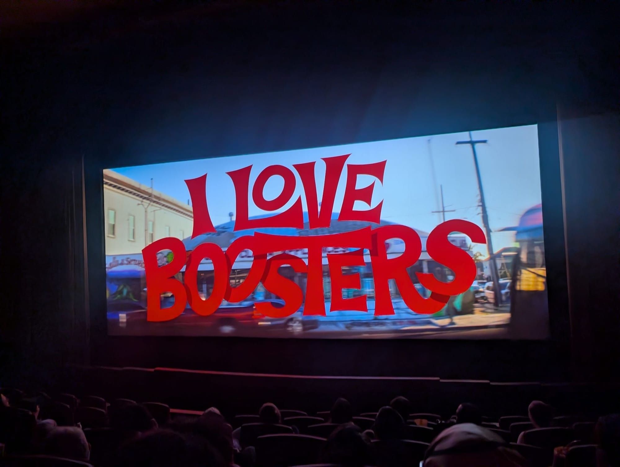 A photo taken during a screening at Grand Lake Theater showing the title screen of "I Love Boosters."