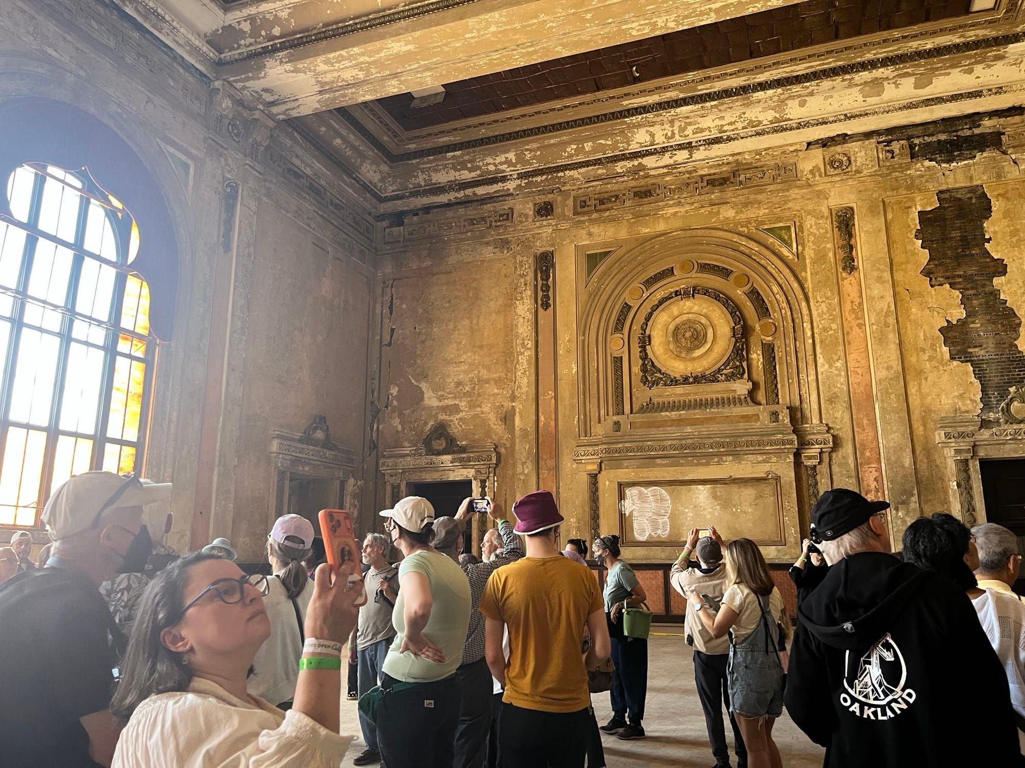 People milling around the interior of the station and taking photos. The walls are crumbling but the old grandeur still evident.