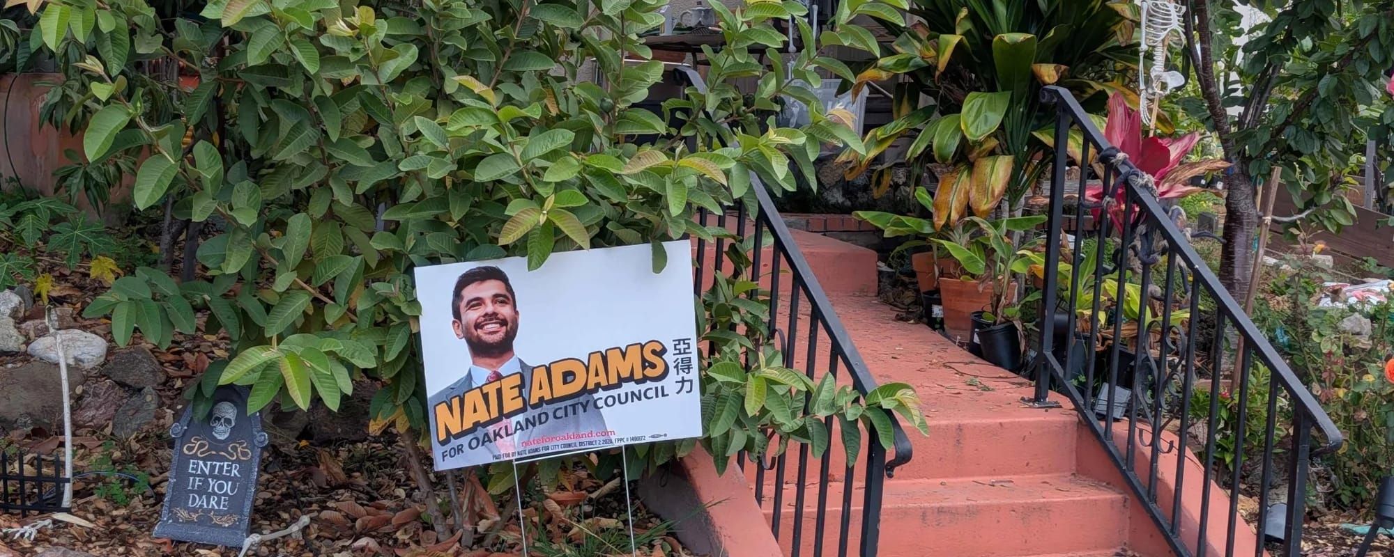 A sign for Nate Adams, with that retro cartoony font, in a yard alongside Halloween decorations, including a metaphorically rich "enter if you dare" sign.