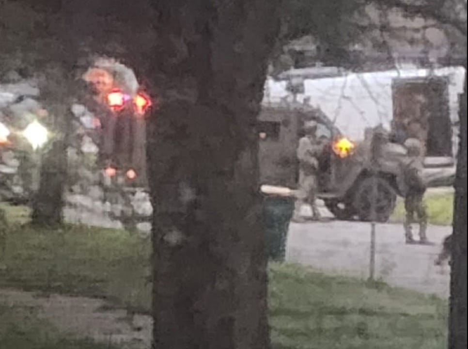 Agents in tactical gear and an armored truck seen through a tree at dawn