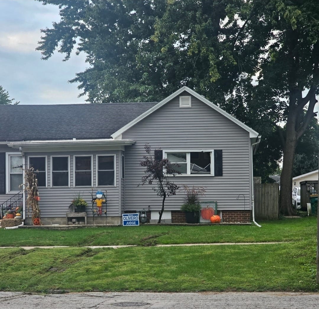 A house with a boarded-up front window and tire ruts across the lawn