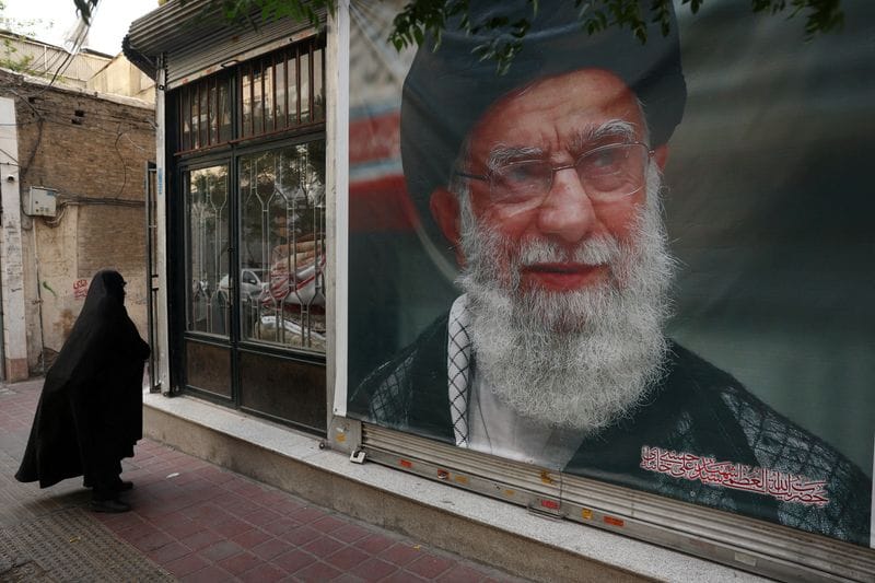 FILE PHOTO: A woman walks past a banner with a picture of the late Iran's Supreme Leader Ayatollah Ali Khamenei, on a street in Tehran