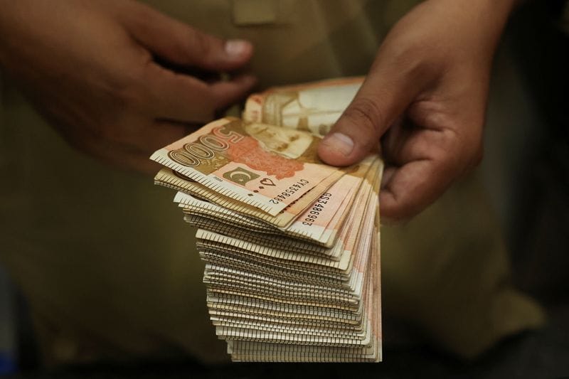 A trader counts Pakistani rupee notes at a currency exchange booth in Peshawar