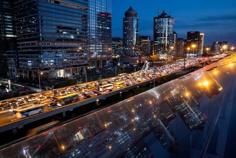Cars are stuck in traffic on an elevated highway as buildings are reflected on a glass surface in Beijing's central business district