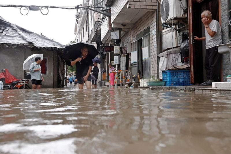 Residents wade through floodwaters at a flooded residential compound amid heavy rainfall brought by Typhoon Dolphin, in Shanghai